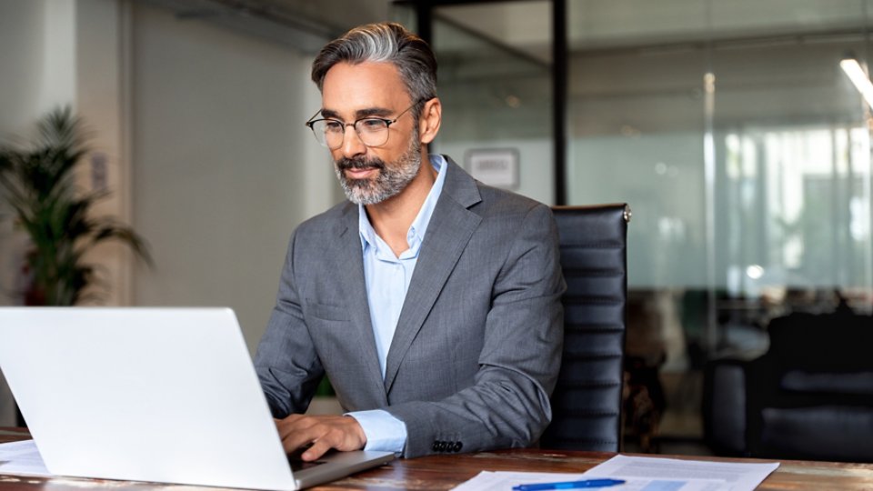 Happy mature European business man ceo trader using computer, typing, working in modern office, doing online data market analysis, thinking planning tech strategy looking at laptop with copy space.