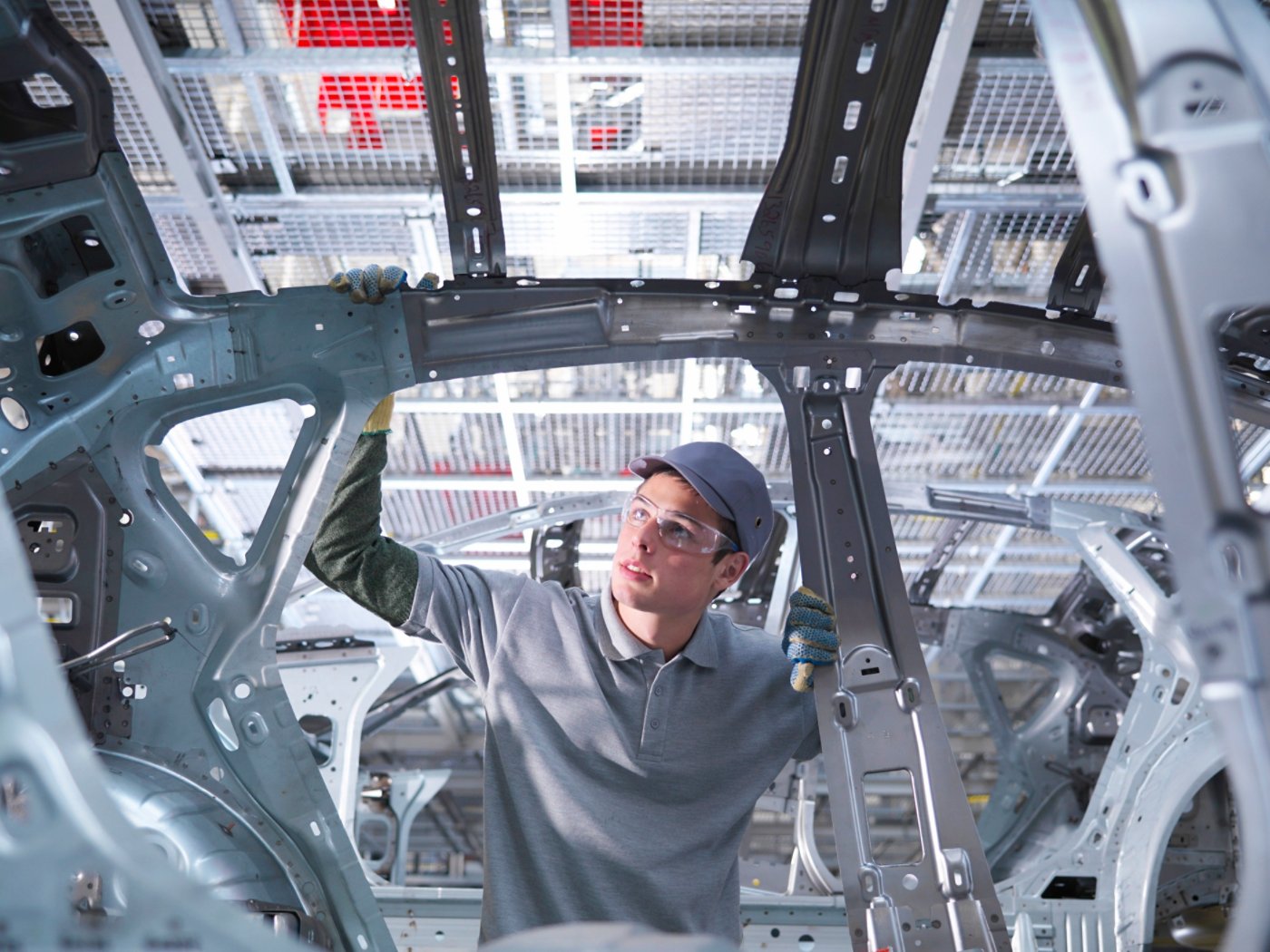 Worker inspecting car at automotive plant.