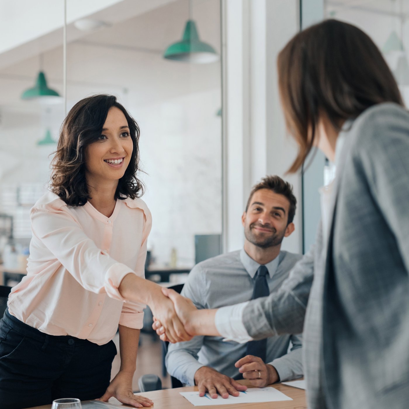 Smiling young businesswoman shaking hands with a coworker during a meeting with colleagues around a table in an office boardroom