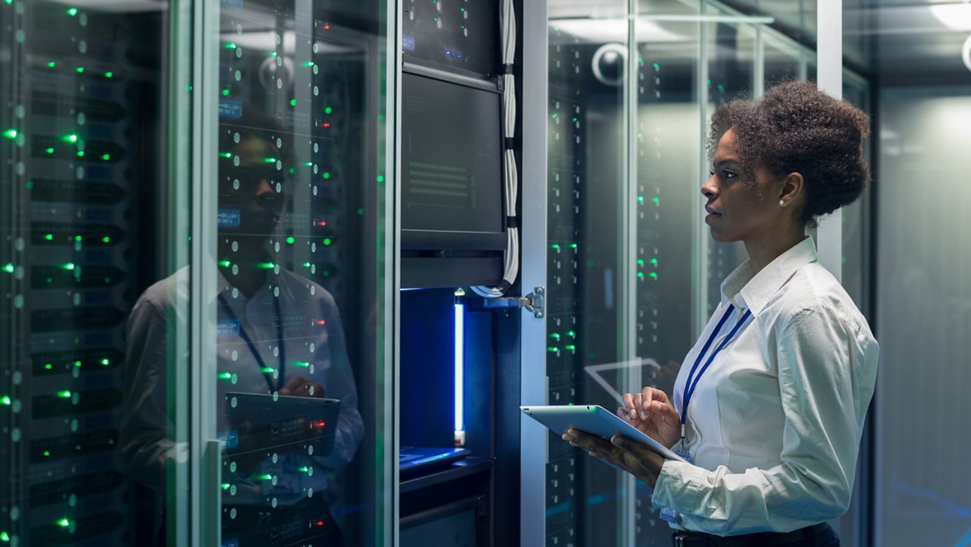 Medium shot of female technician working on a tablet in a data center full of rack servers running diagnostics and maintenance on the system