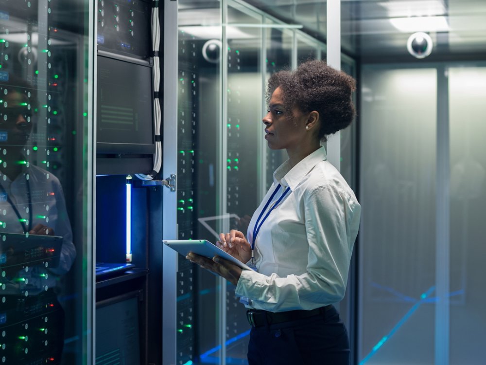 Medium shot of female technician working on a tablet in a data center full of rack servers running diagnostics and maintenance on the system