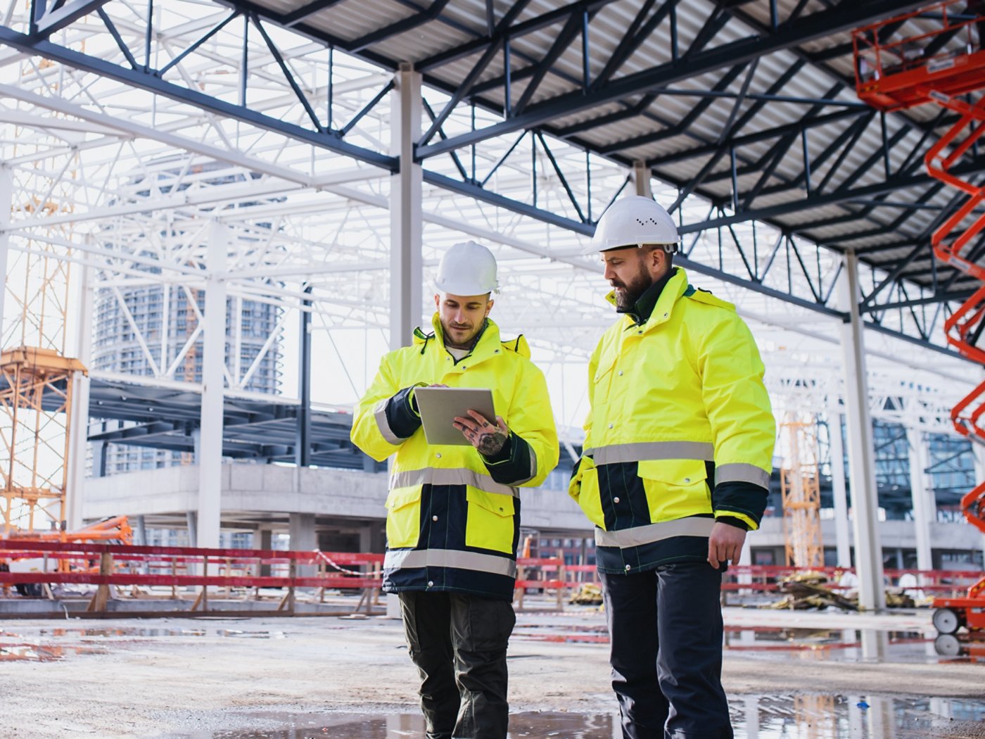 Men engineers standing outdoors on construction site, using tablet. Copy space.