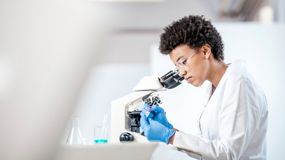 African American woman looking through a microscope in a lab