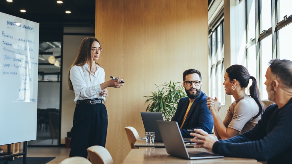 Confident young businesswoman discussing her marketing strategy and ideas with her team. Female manager giving a presentation during a meeting with her colleagues in a modern workspace.