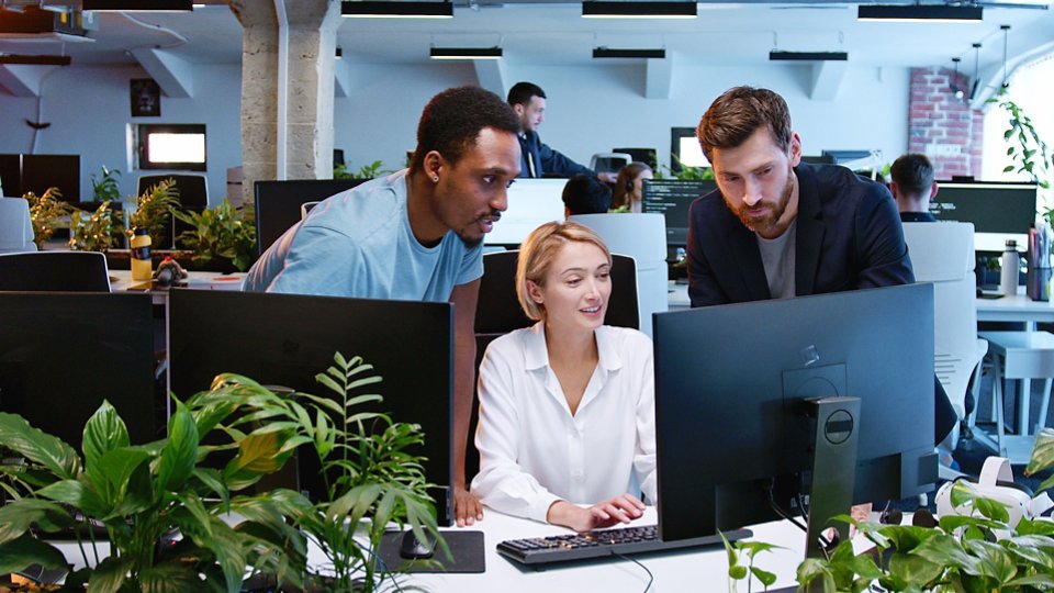 Woman with coworkers discussing working project at computer in coworking space. Multiethic team of developers talking and giving advices. Workday in office. Business concept. Communication. Management