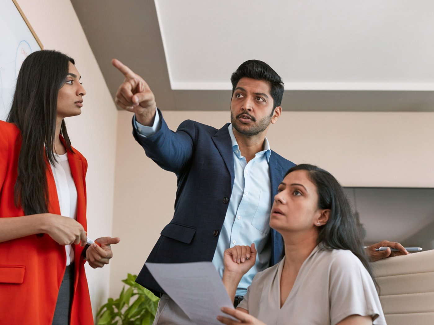 Three business people looking at a white board and discussing 4X3