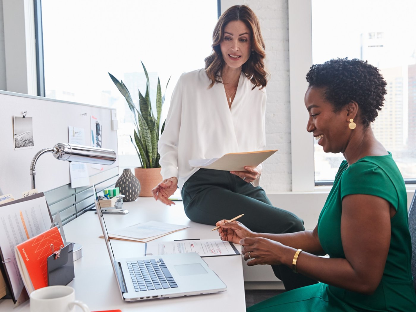 Two multi ethnic business women having a casual work discussion at a desk 4X3