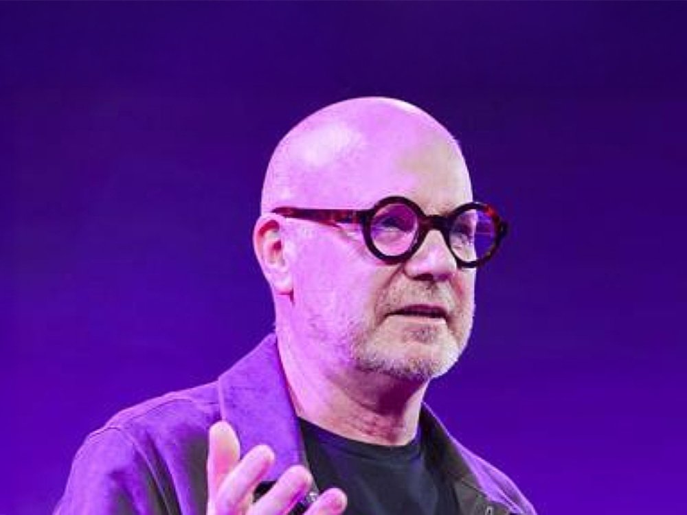 Man gesturing on stage with purple backdrop