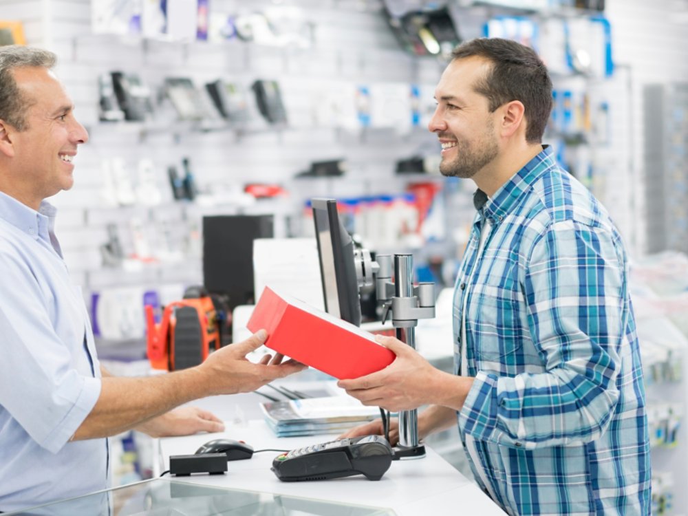 Casual man shopping at a tech store and talking to salesman over the counter