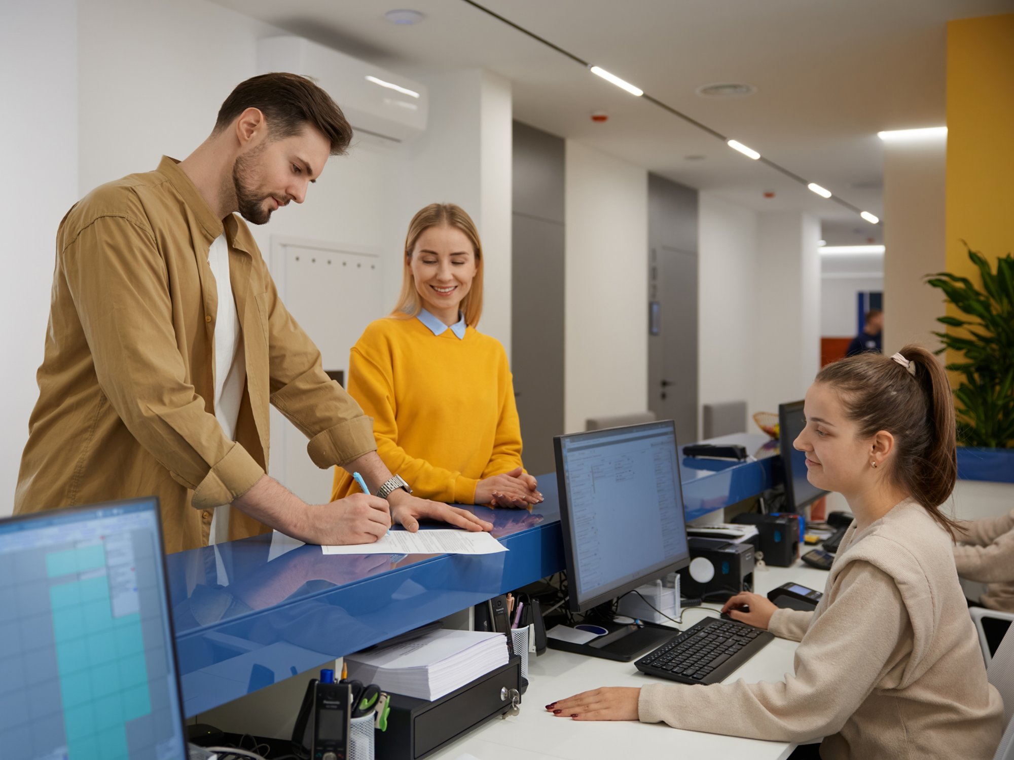 Man and woman couple signing paper documents at modern clinic reception desk. Young family filling questionnaire before doctor appointment while visiting hospital