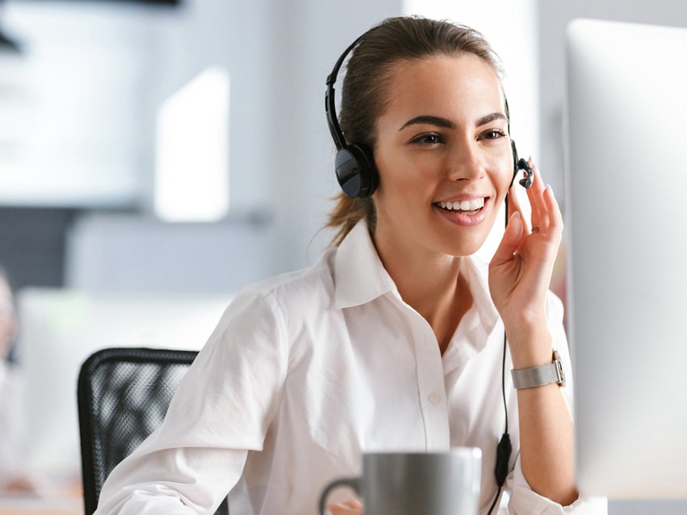 Emotional business woman in office callcenter working with computer wearing headphones.