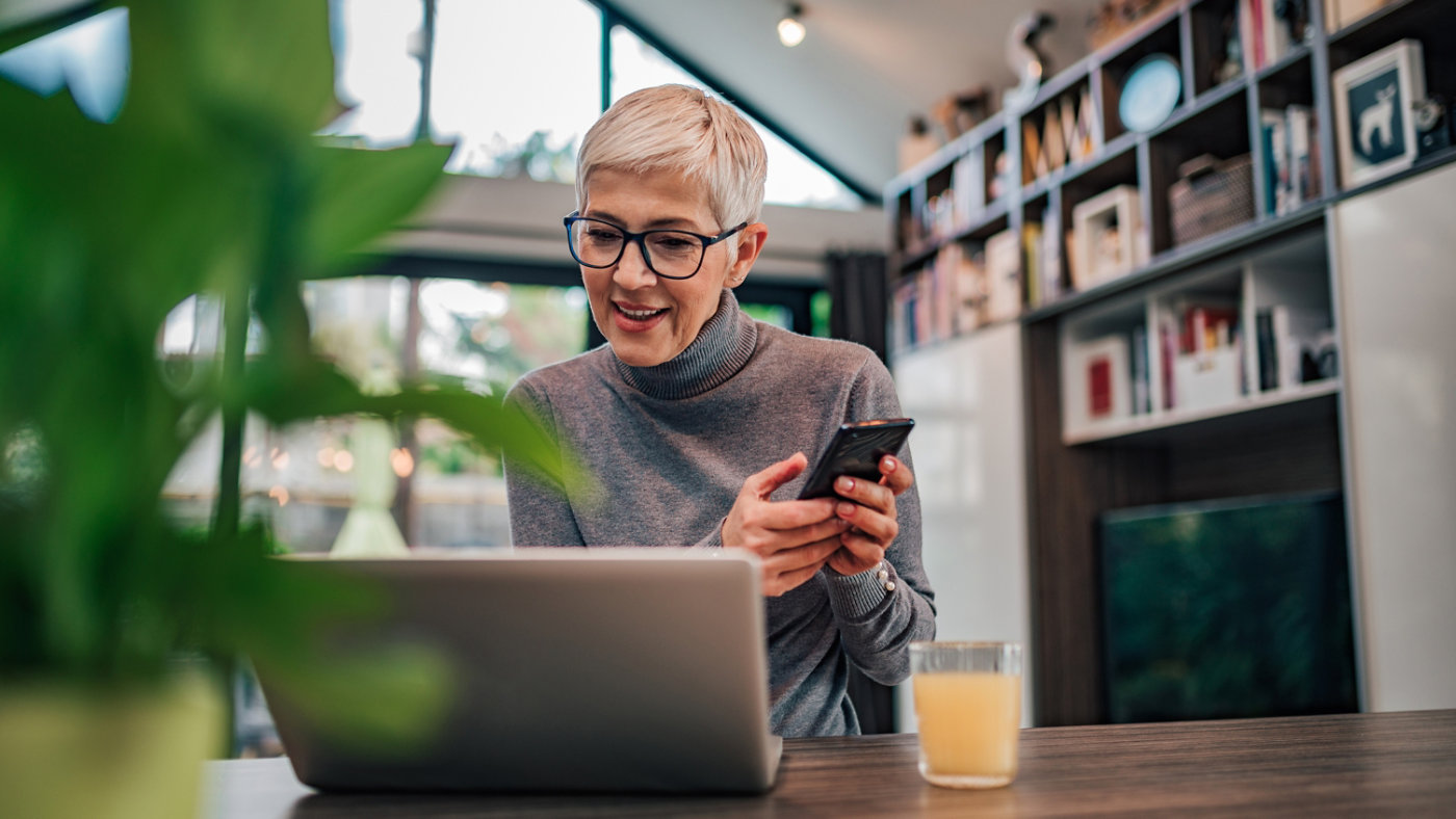 Modern senior woman using smart phone and laptop, portrait. 16x9