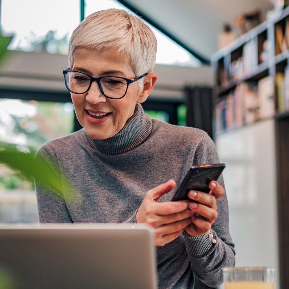 Modern senior woman using smart phone and laptop, portrait.