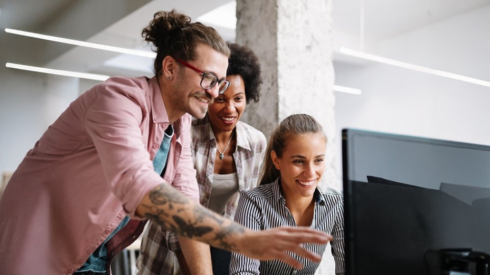 Three coworkers discussing a business project that is presented on a computer screen