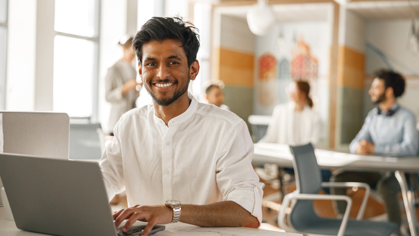 Smiling Businessman working laptop while sitting in modern office on colleagues background