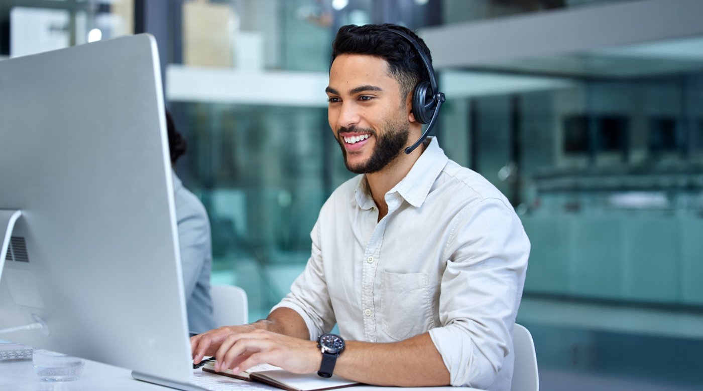 Business man, call center and web support communication at a computer in a office. Phone conversation, smile and male worker with contact us, crm and customer service job in a consulting agency