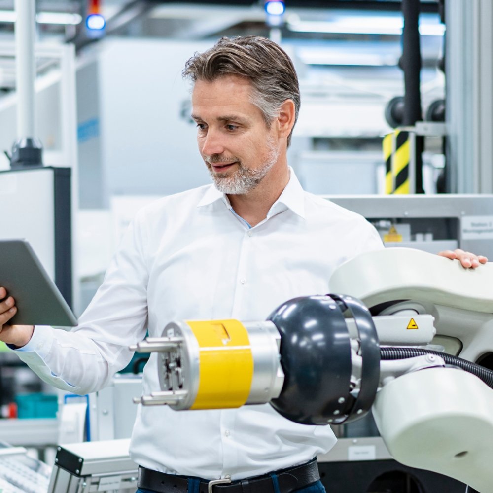 Businessman with tablet at assembly robot in a factory