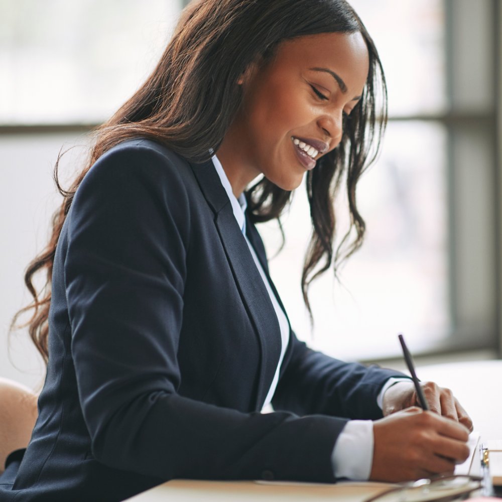Smiling young African American businesswoman writing down notes in her day planner while sitting at a table in an office