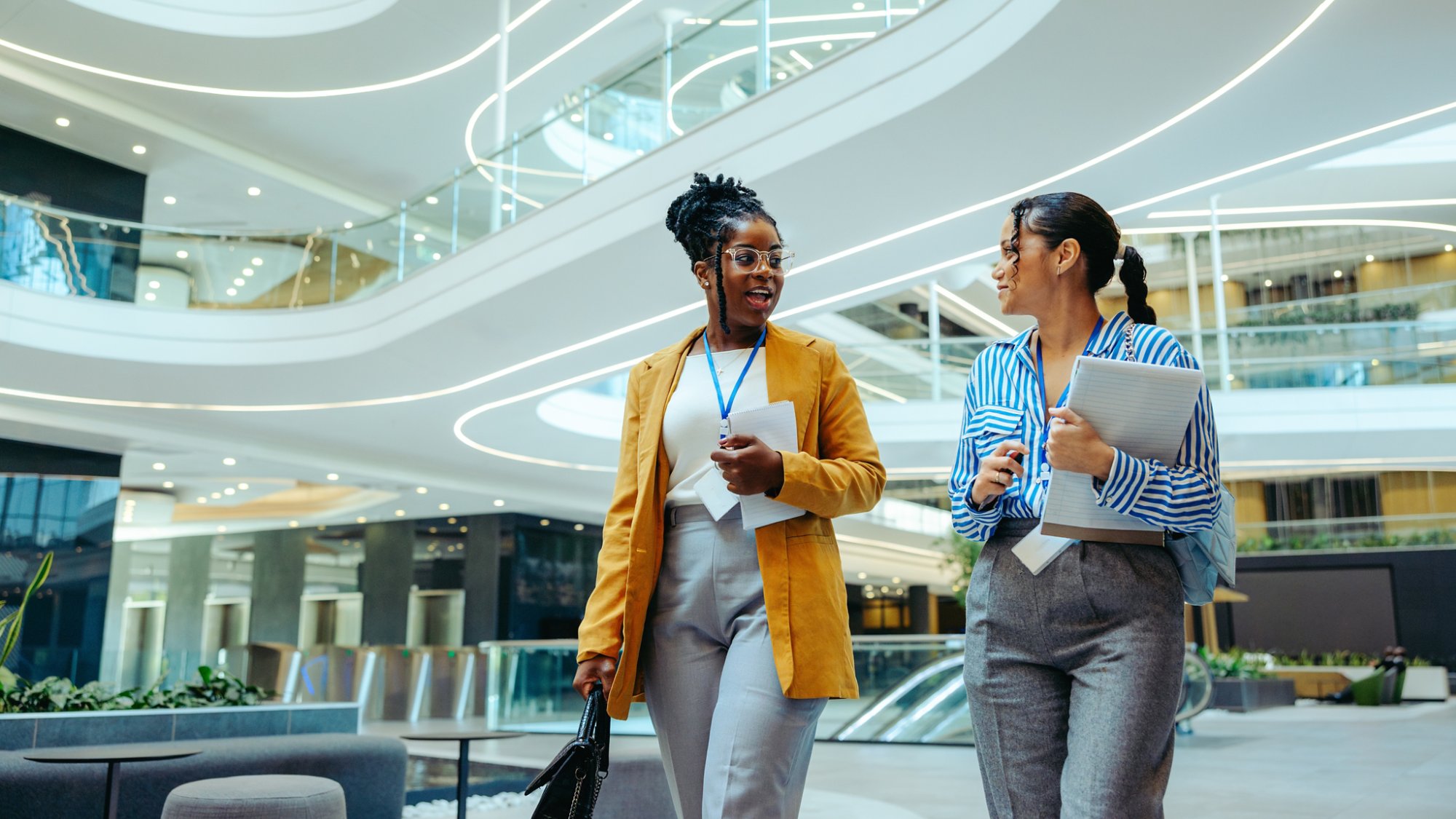 Two female auditors walking in a modern office, discussing financial advisory and consulting. Professional career advancement and corporate environment.