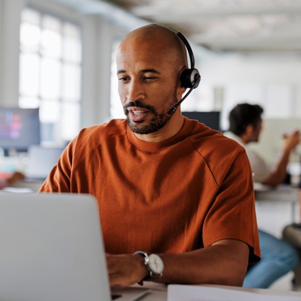 Customer service agent is handling a call while typing on his laptop in a busy office