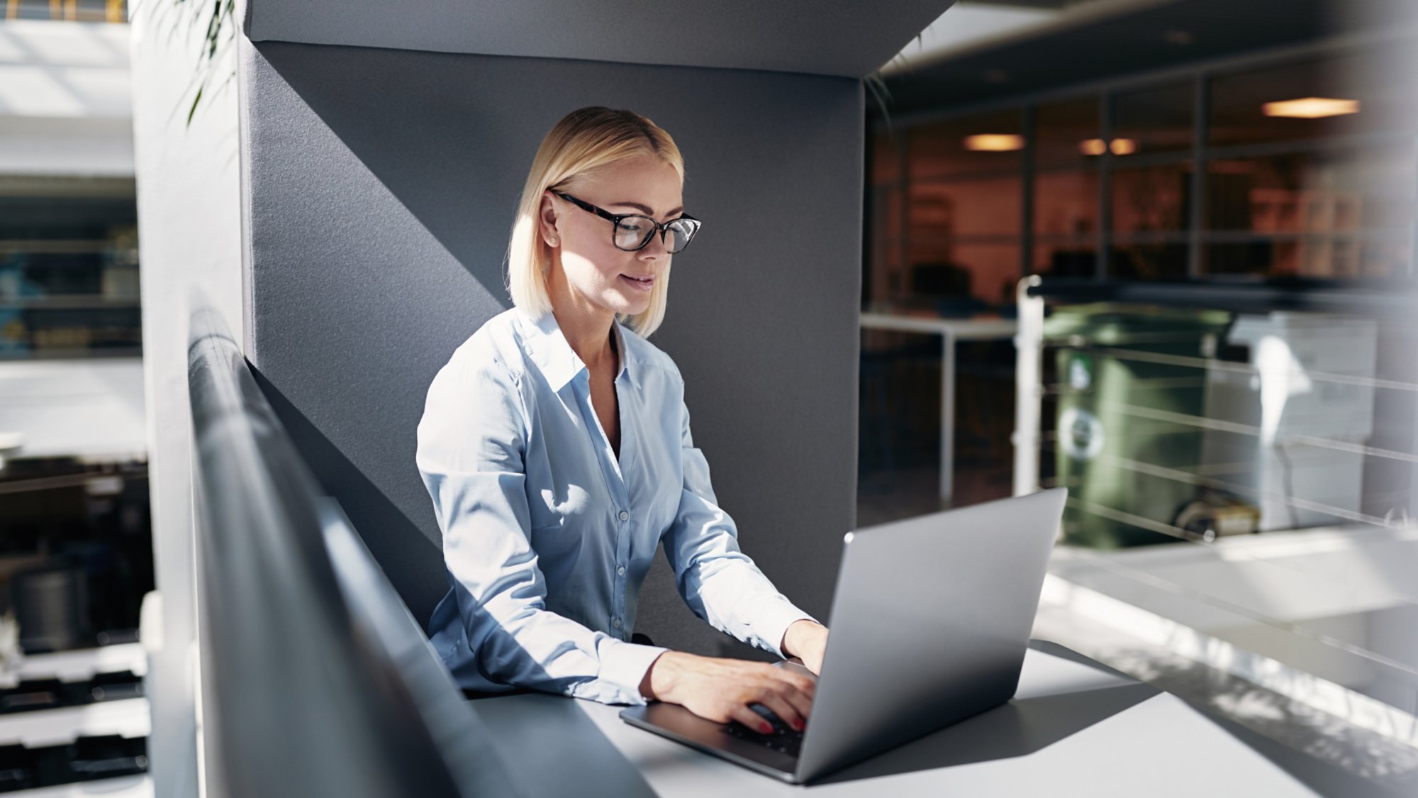 Smiling young businesswoman working online with a laptop while sitting alone in an office pod