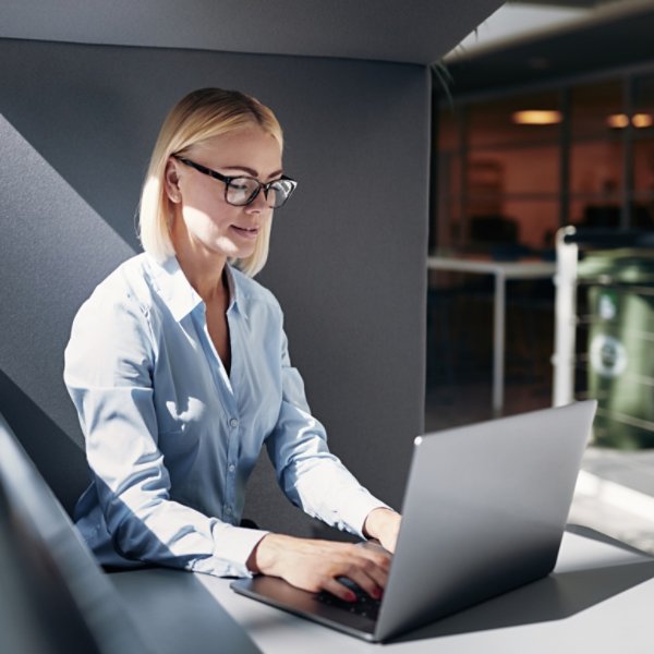 Smiling young businesswoman working online with a laptop while sitting alone in an office pod