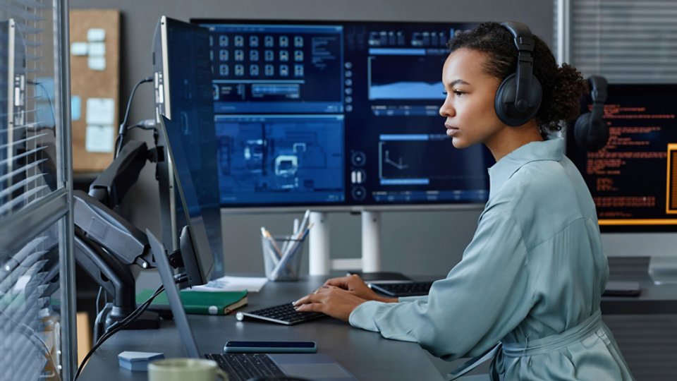 Young computer programmer wearing wireless headphones working on desktop PC