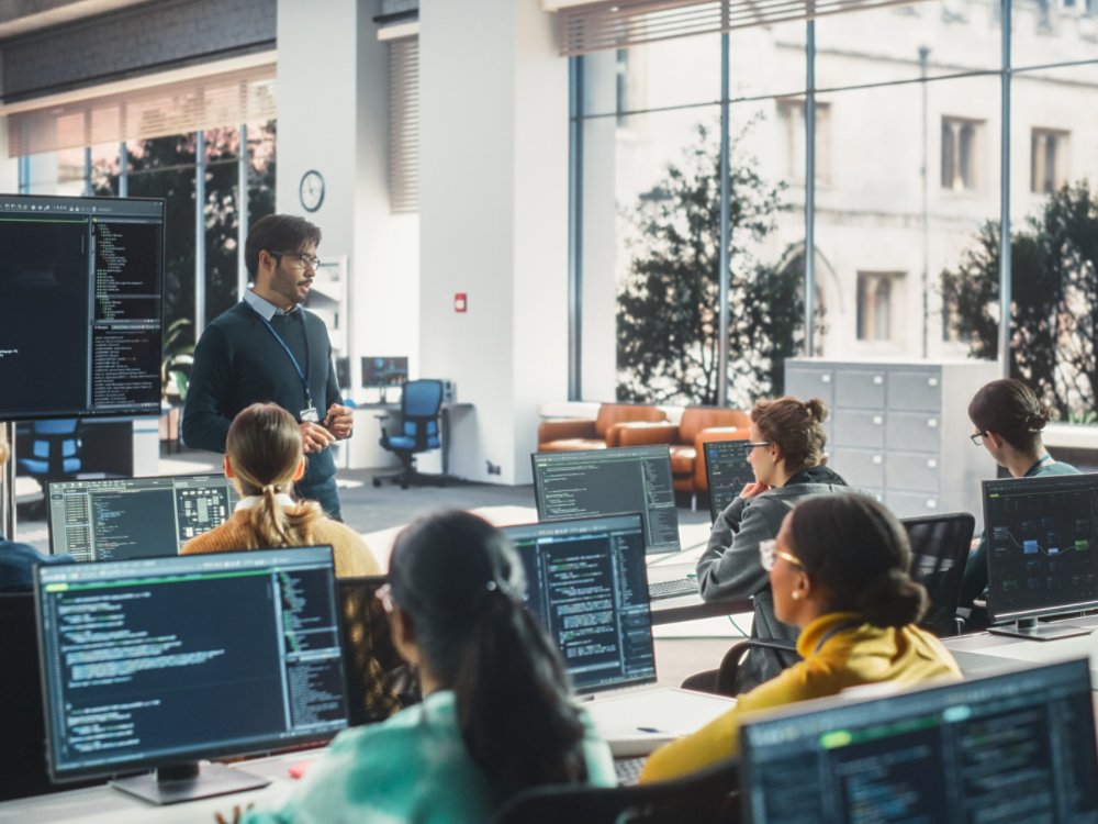 Teacher Giving Lesson to Diverse Multiethnic Group of Female and Male Students in College Room. Class Learning About Computer Science and Software Development. Lecturer Shares Knowledge with Scholars