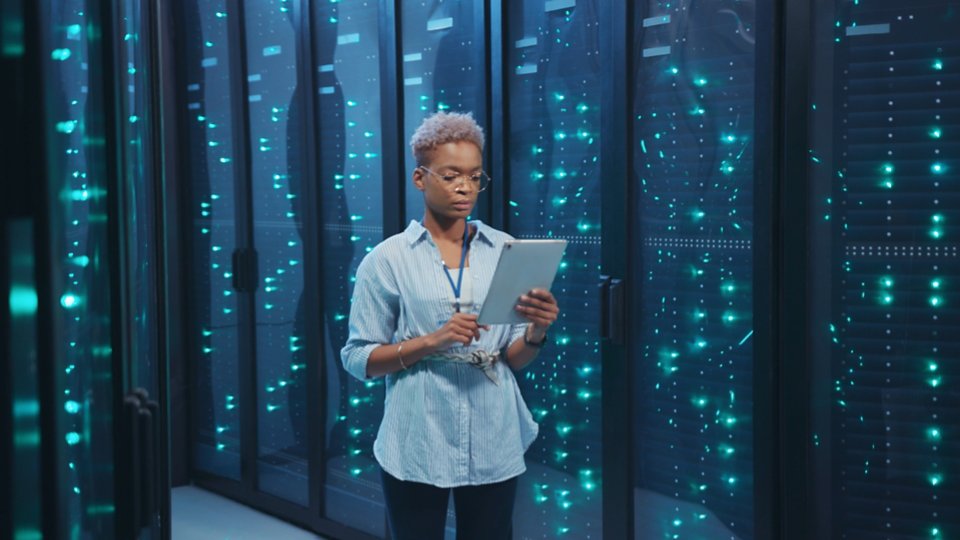 Afro-american female IT administrator walking in server corridor diagnosing hardware system performance in data center cyber secure storage.