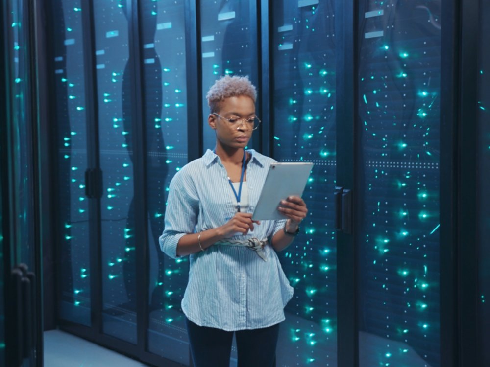 Afro-american female IT administrator walking in server corridor diagnosing hardware system performance in data center cyber secure storage.