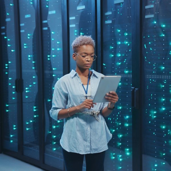 Afro-american female IT administrator walking in server corridor diagnosing hardware system performance in data center cyber secure storage.