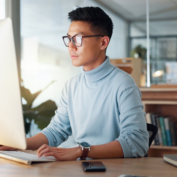 Asian man at computer, glasses and ideas, thinking and reading email, web review or article at digital agency. Research, reflection and businessman at tech startup networking on business website