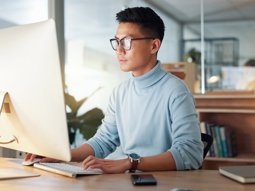 Asian man at computer, glasses and ideas, thinking and reading email, web review or article at digital agency. Research, reflection and businessman at tech startup networking on business website