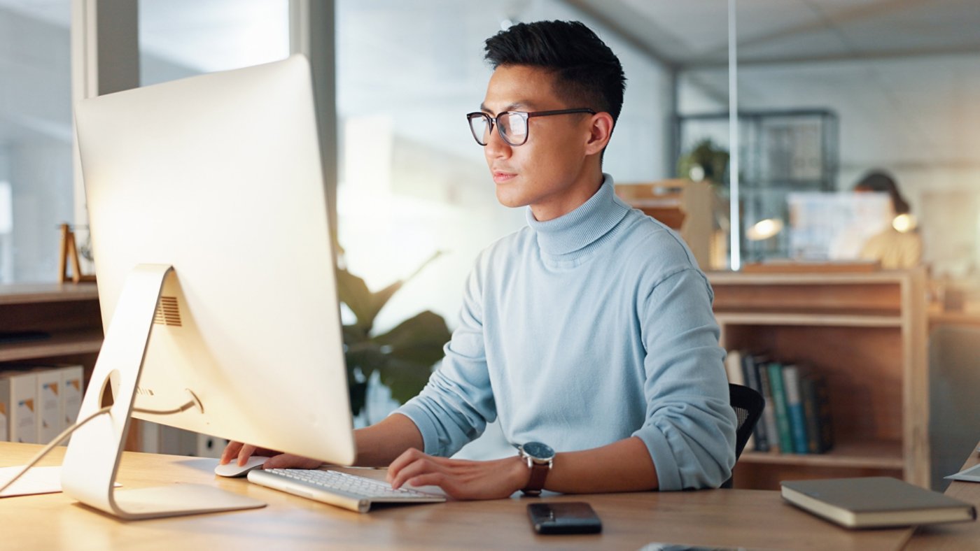 Asian man at computer, glasses and ideas, thinking and reading email, web review or article at digital agency. Research, reflection and businessman at tech startup networking on business website