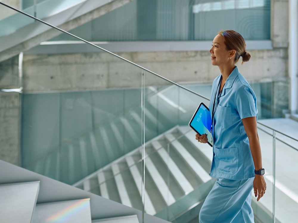 Confident doctor walking up stairs in modern hospital holding tablet