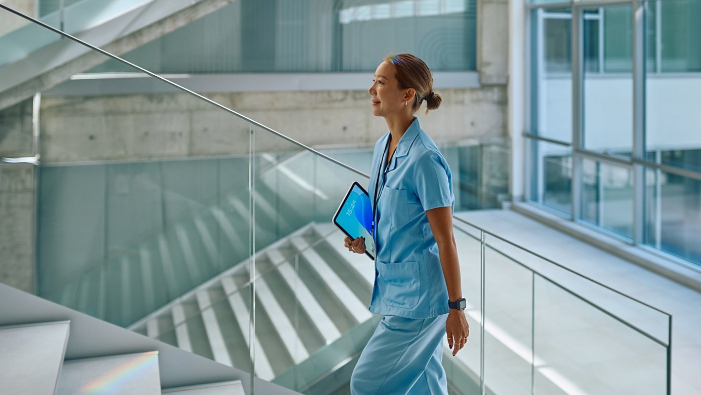 Confident doctor walking up stairs in modern hospital holding tablet