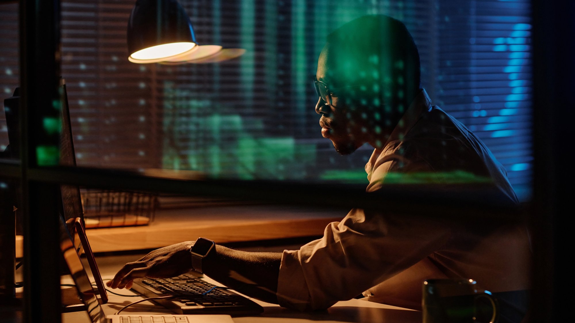 African American programmer concentrating on his work on computer he working overtime in dark office
