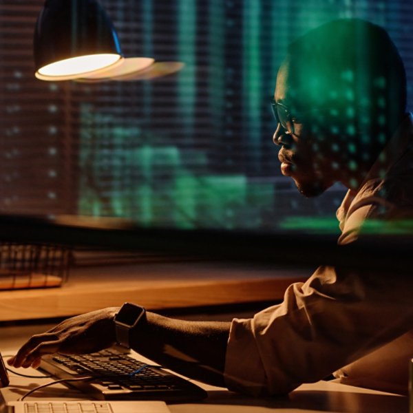 African American programmer concentrating on his work on computer he working overtime in dark office