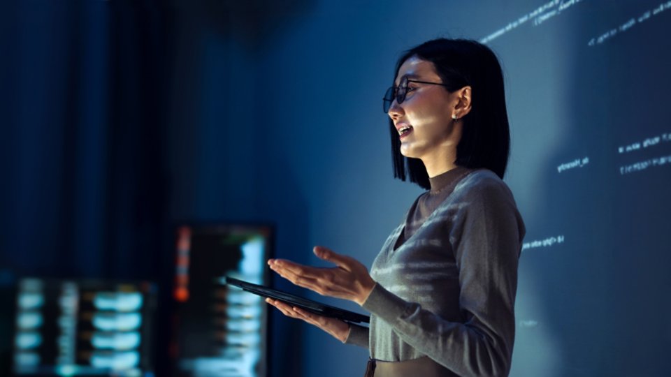 asian woman programmer standing in front of a screen with code projected  presentation the integration of technology and human expertise in software development
