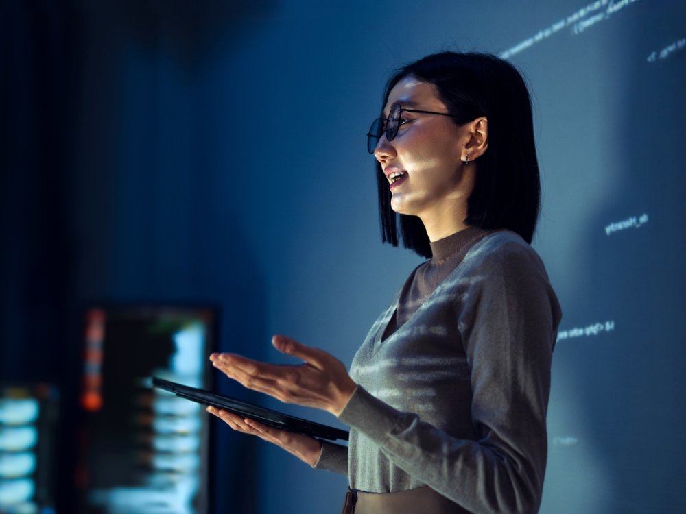 asian woman programmer standing in front of a screen with code projected  presentation the integration of technology and human expertise in software development