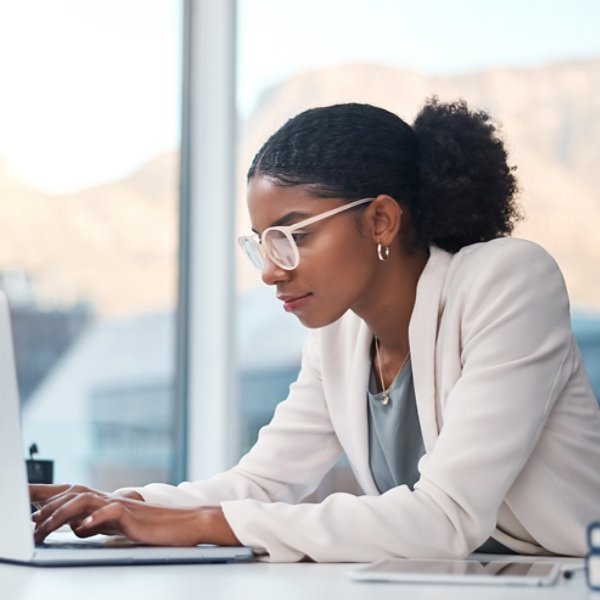 Data professional and secretary typing an email on a laptop and doing online research while working in an office. African entrepreneur looking focused while using the internet for work.