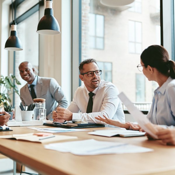 Group of diverse businesspeople smiling while discussing paperwork together during a meeting around a table in a modern office