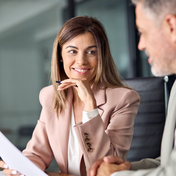 Two business executives discussing financial legal papers in office at meeting. Smiling female lawyer adviser consulting mid aged client at meeting. Mature colleagues doing project paperwork overview.