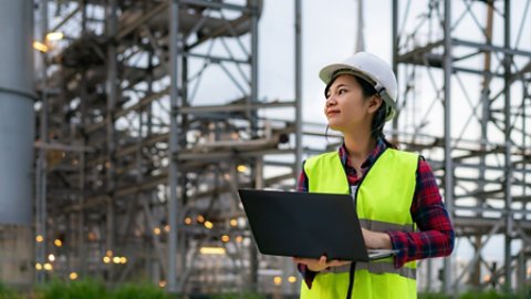 Asian woman petrochemical engineer working at night with laptop Inside oil and gas refinery plant industry factory at night for inspector safety quality control.
