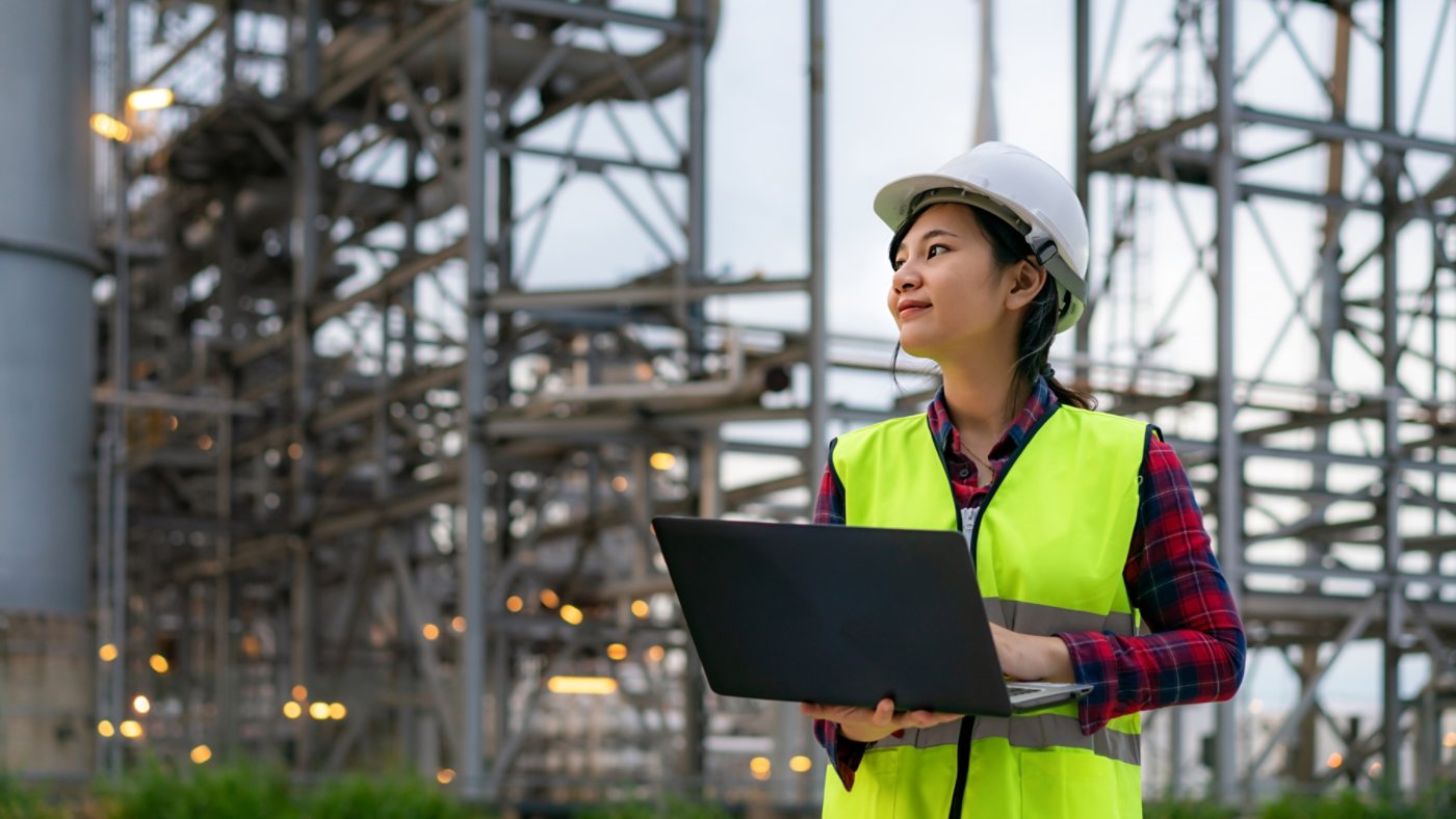 Asian woman petrochemical engineer working at night with laptop Inside oil and gas refinery plant industry factory at night for inspector safety quality control.