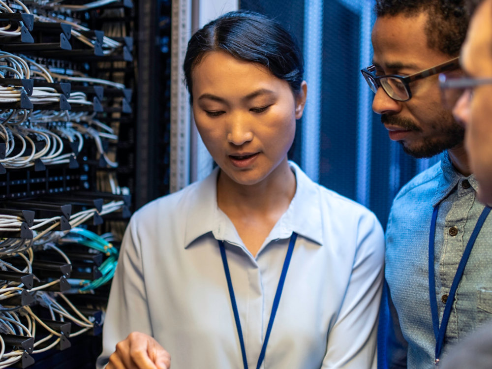 Three IT technician looking at a digital tablet and talking while standing next to a server in a data center.