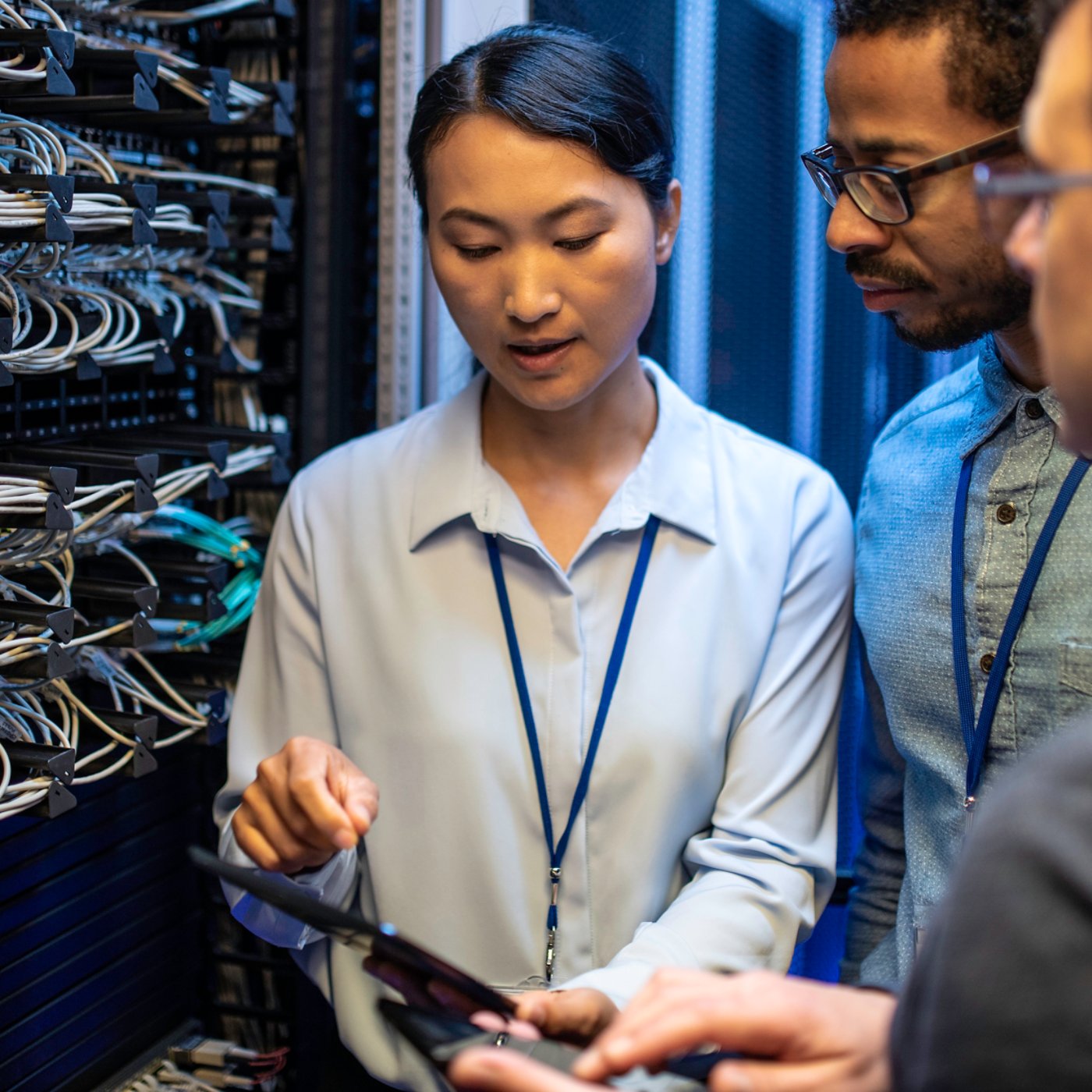 Three IT technician looking at a digital tablet and talking while standing next to a server in a data center 1X1