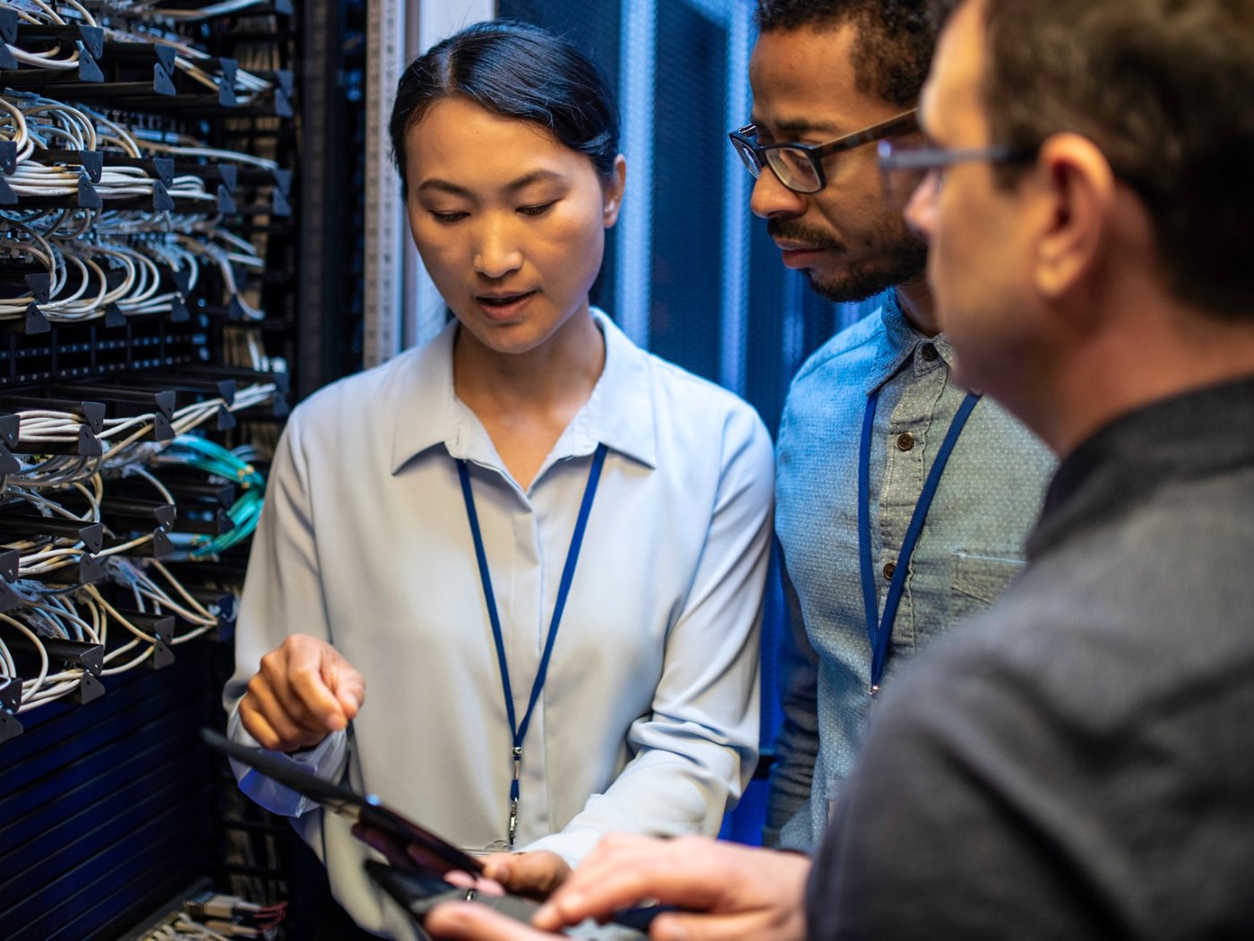 Three IT technician looking at a digital tablet and talking while standing next to a server in a data center.