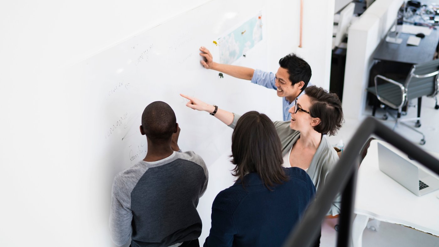 A photo of business people communicating over transparent board. High angle view of multi-ethnic professionals are planning in creative office. They are wearing smart casuals at workplace.