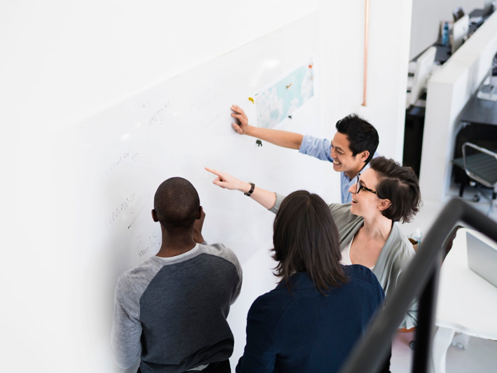 A photo of business people communicating over transparent board. High angle view of multi-ethnic professionals are planning in creative office. They are wearing smart casuals at workplace.